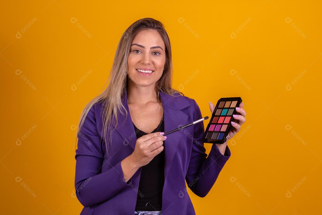 Mulher loira com um blazer roxo passando maquiagem