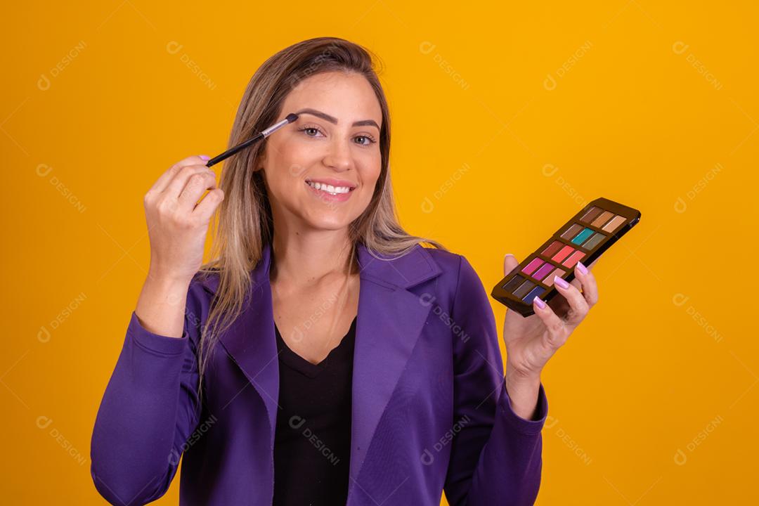 Mulher loira com um blazer roxo passando maquiagem