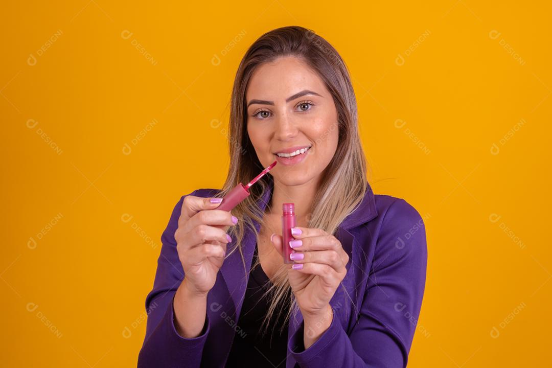 Mulher loira com um blazer roxo passando batom