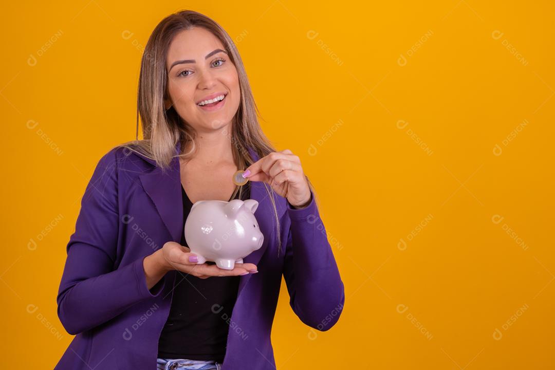 Mulher loira colocando moedas em porquinho para poupar
