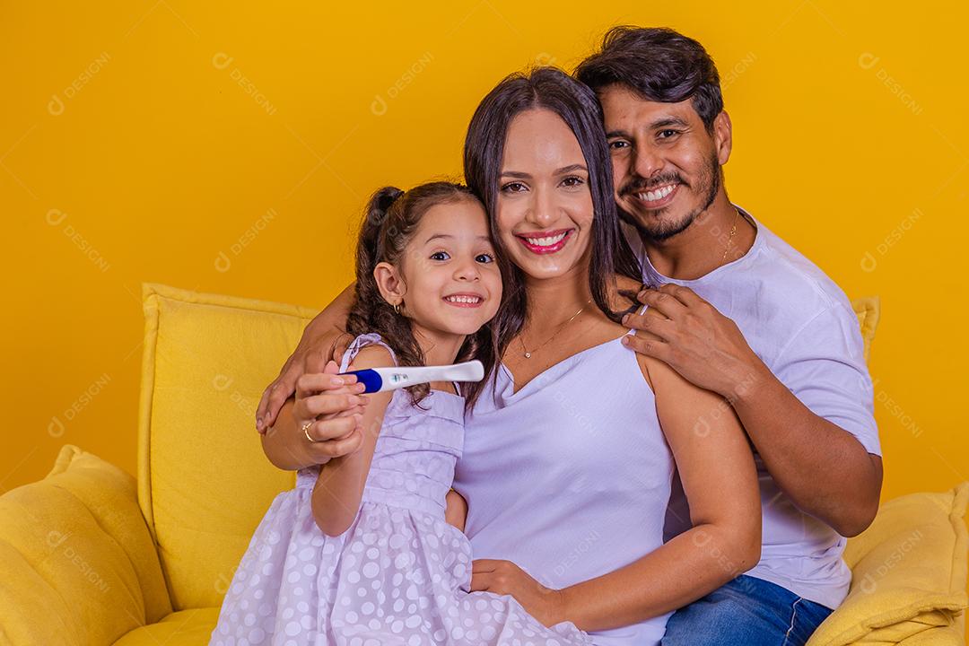 Futura irmã mais velha segurando um teste de gravidez positivo com sua família em crescimento. Feliz mãe, pai e filha com teste de gravidez positivo.