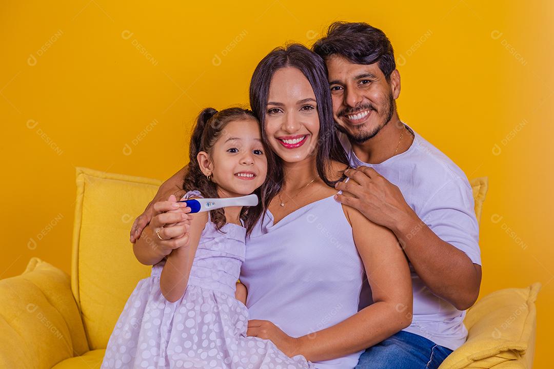 Futura irmã mais velha segurando um teste de gravidez positivo com sua família em crescimento. Feliz mãe, pai e filha com teste de gravidez positivo.