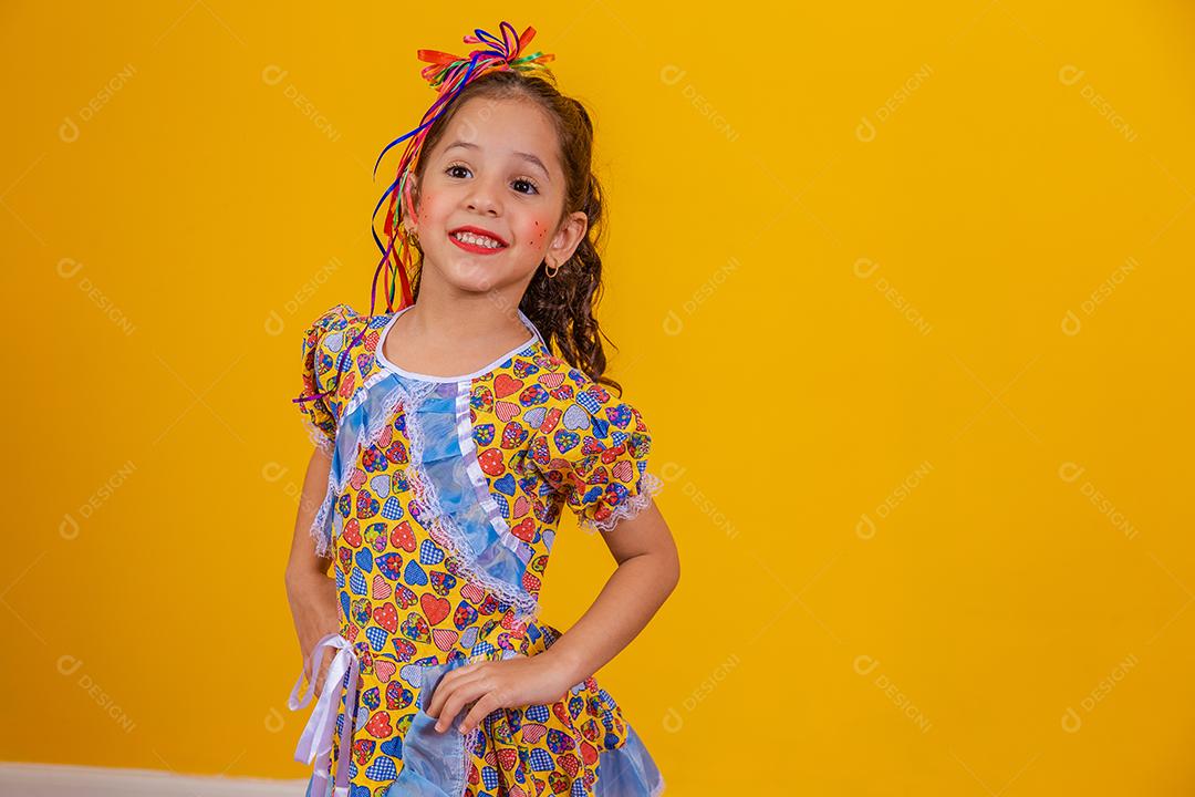 Criança com roupas típicas da famosa festa brasileira chamada Festa Junina em comemoração ao São João. Linda garota em fundo amarelo.