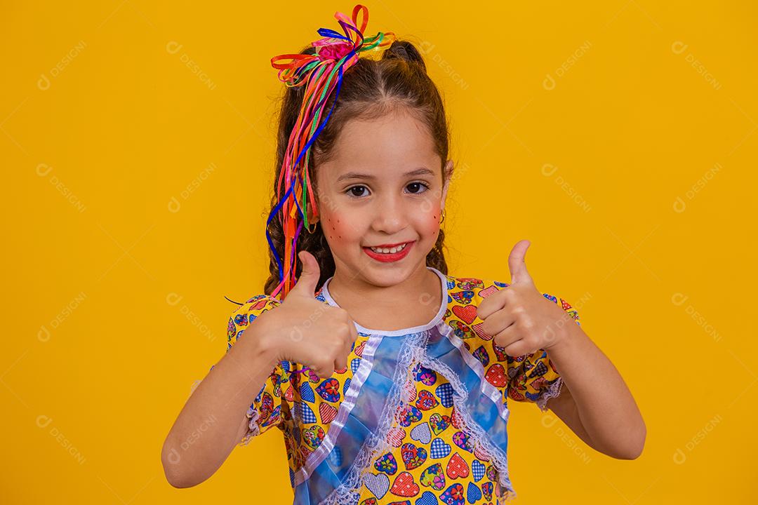 Menina bonitinha com o polegar para cima vestida com roupa de festa junina.