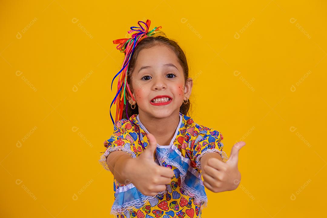 Menina bonitinha com o polegar para cima vestida com roupa de festa junina.