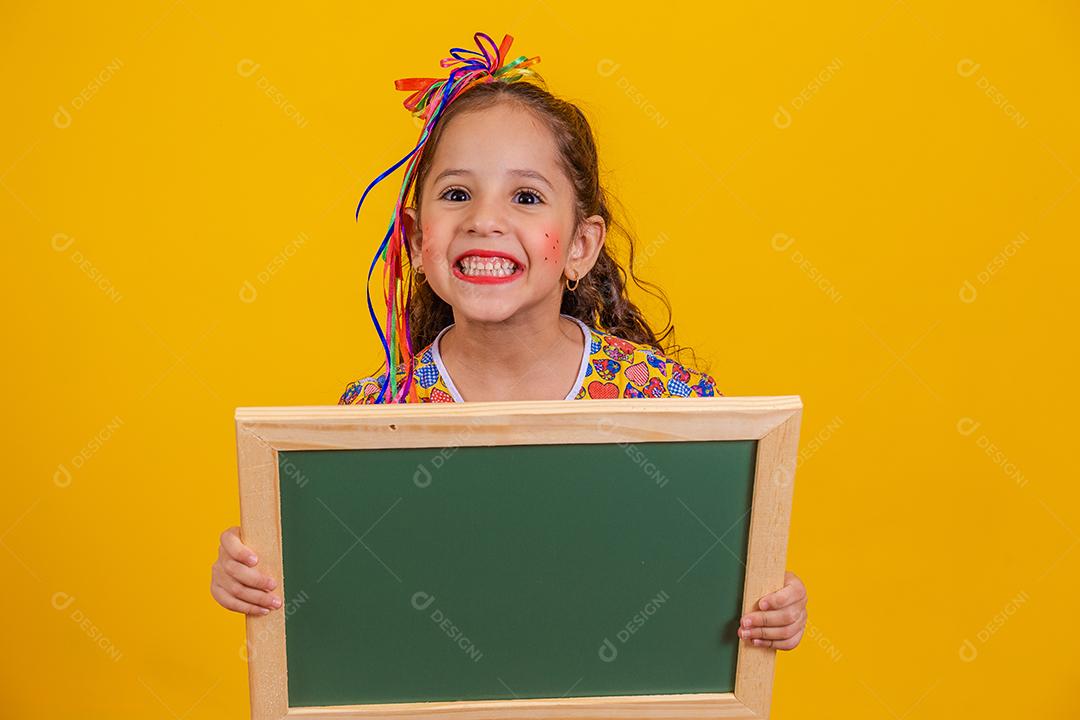 Linda garotinha vestida com roupa típica de festa junina com um quadro-negro