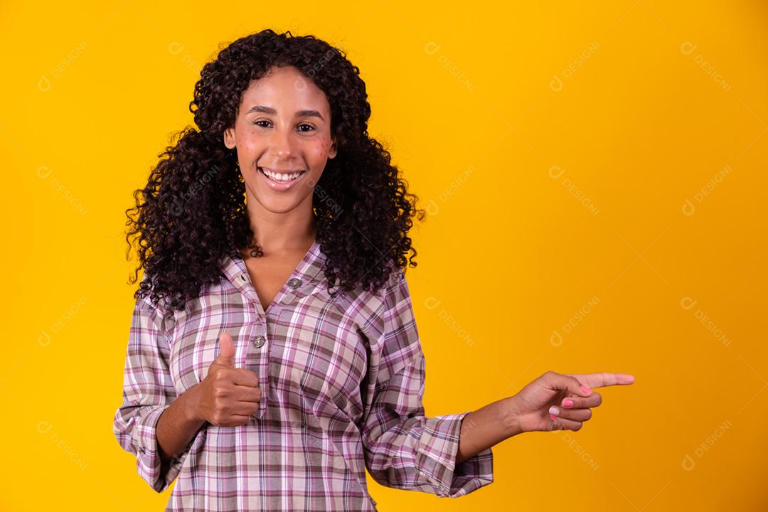 Mulher afro vestida com roupa de festa junina apontando para o lado.
