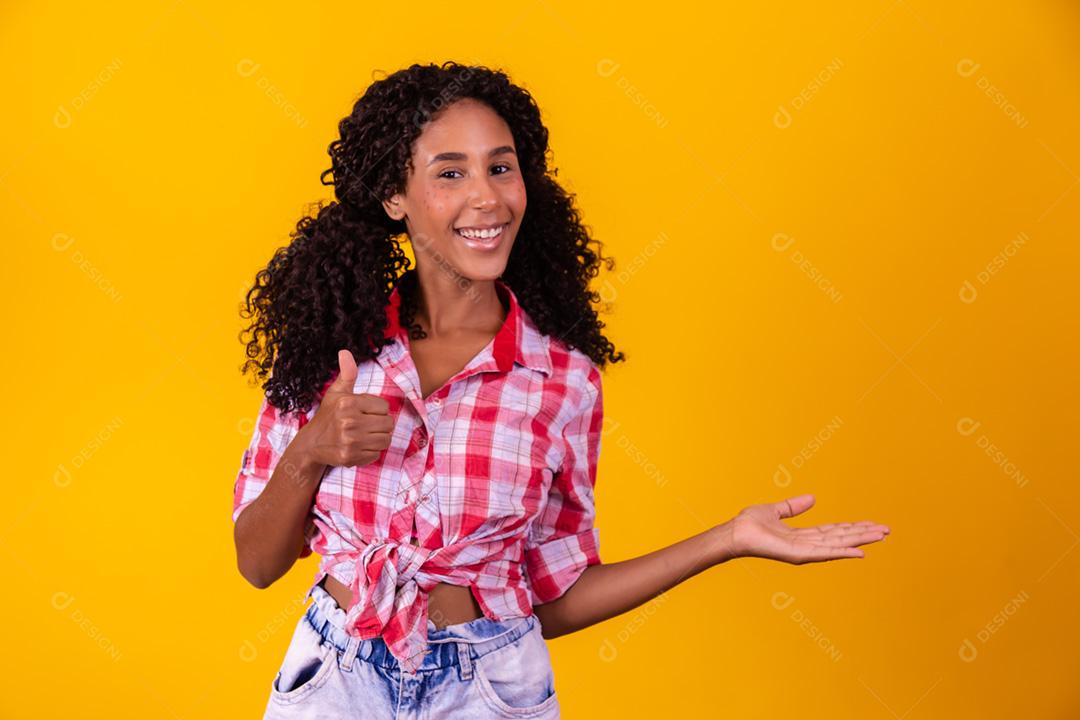 Mulher afro vestida com roupa de festa junina apontando para o lado.
