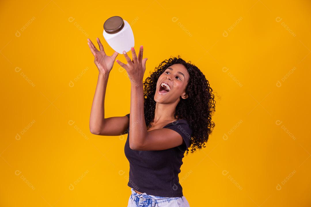 linda garota afro com cabelos cacheados com uma garrafa de creme hidratante