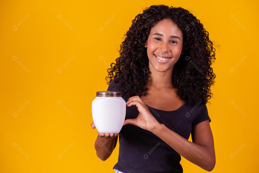 linda garota afro com cabelos cacheados com uma garrafa de creme hidratante