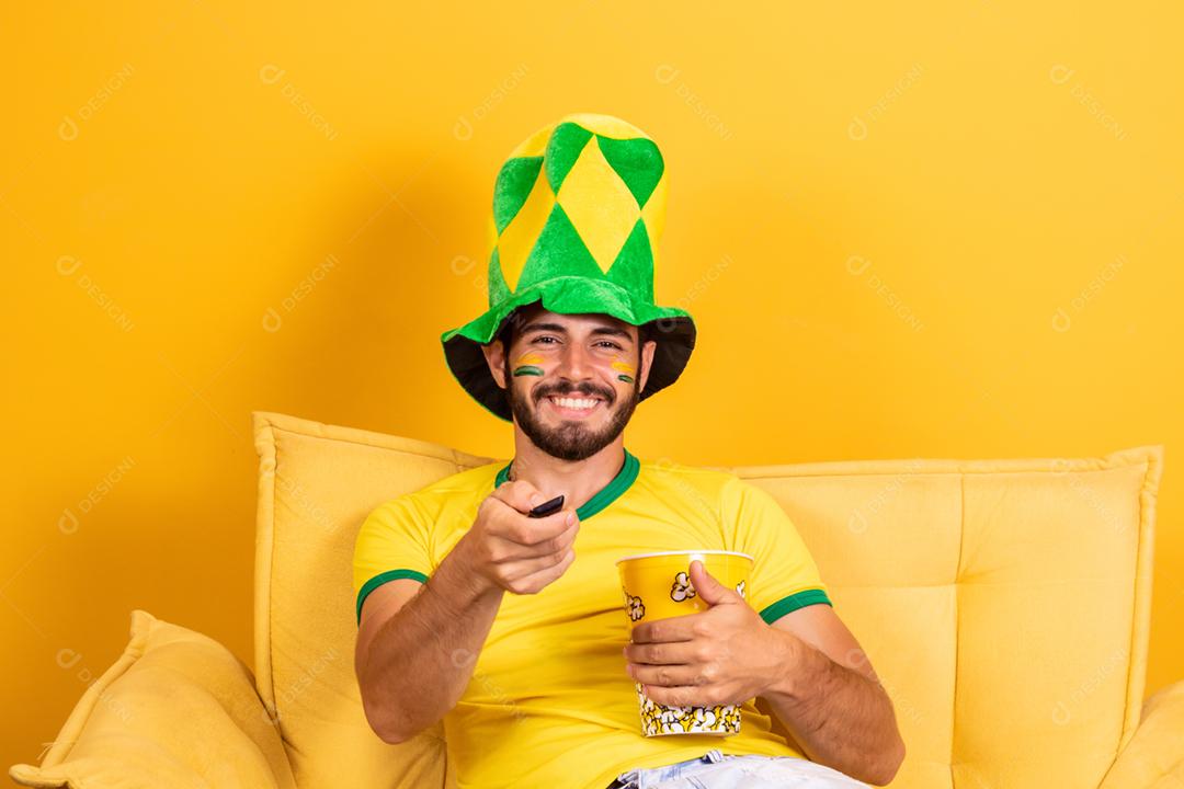 Jovem fã brasileiro assistindo o jogo na tv segurando um controle remoto