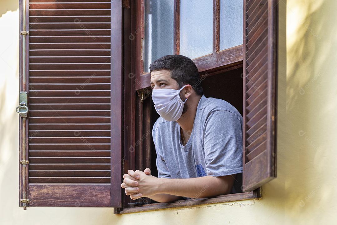 homem com masacara de prteção na janela de casa