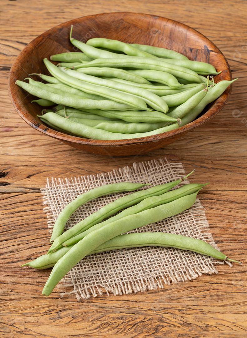 Um grupo de vagens de feijão verde em uma tigela sobre a mesa de madeira.
