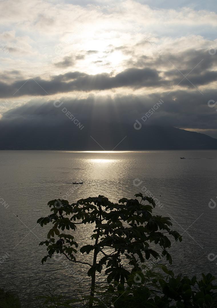 Silhueta de árvores e mar dourado ao pôr do sol na ilha de Ilhabela, Brasil.