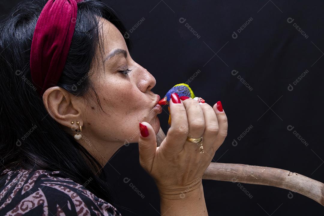 mulher beijando pássaro colorido em imagem com fundo ecuro