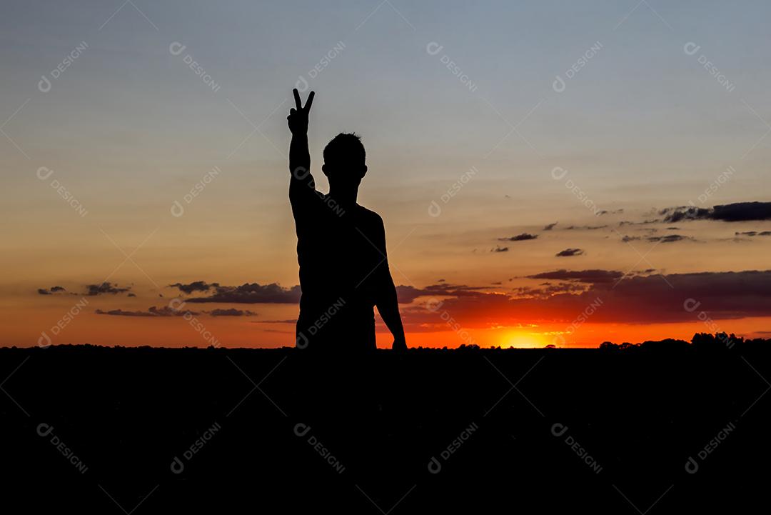 Silhueta do sol com menino mostrando a mão com símbolo de paz e amor