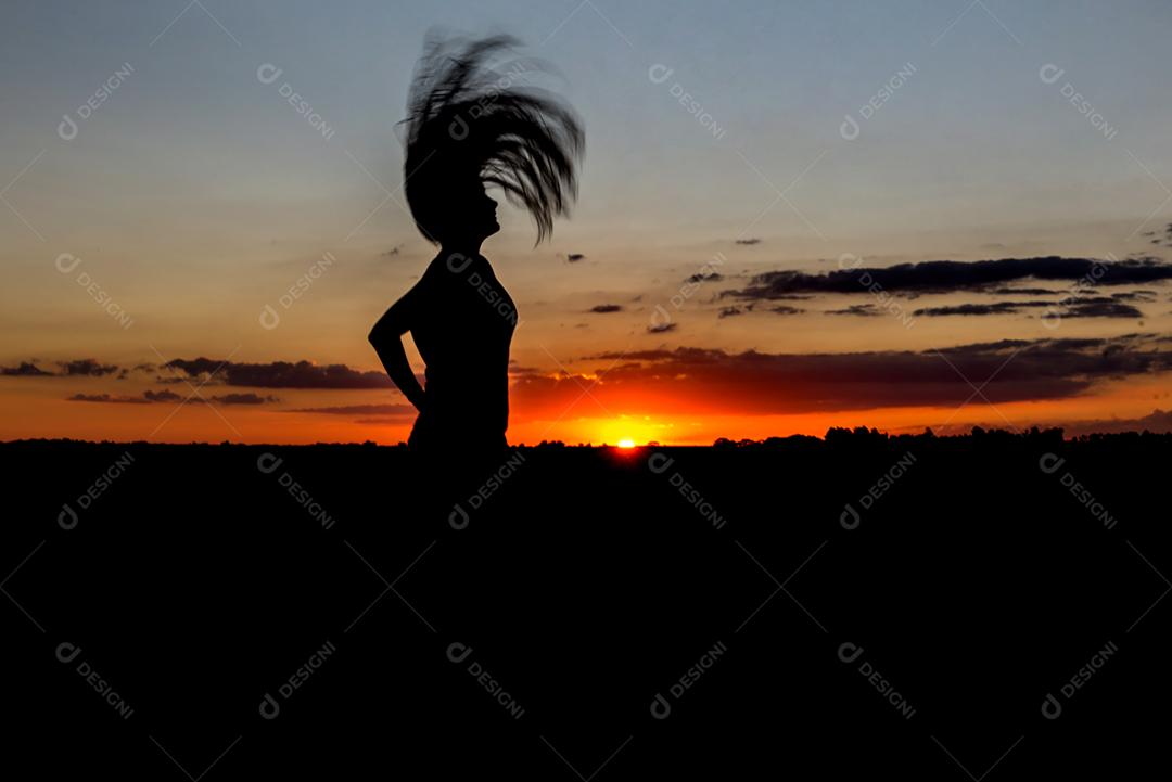 Pôr do sol com silhueta feminina com cabelo vomitando.