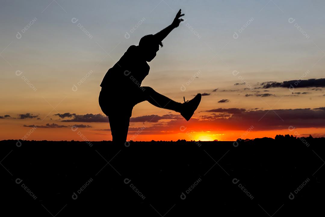 Belo pôr do sol com silhueta de menino pulando de alegria.