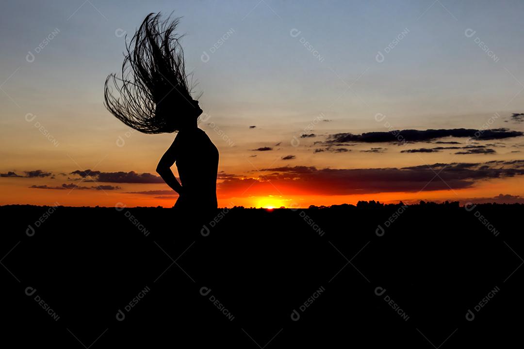 Belo pôr do sol com silhueta de menina pulando com o cabelo