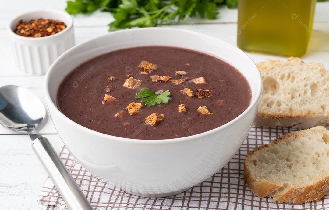 Sopa de feijão preto em uma tigela com fatias de pão e tempero sobre w