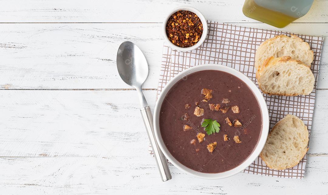 Sopa de feijão preto em uma tigela com fatias de pão e tempero sobre w