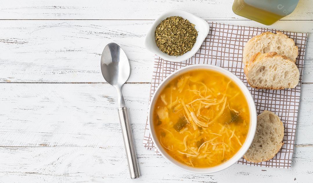 Sopa de galinha em uma tigela com fatias de pão e tempero sobre madeira