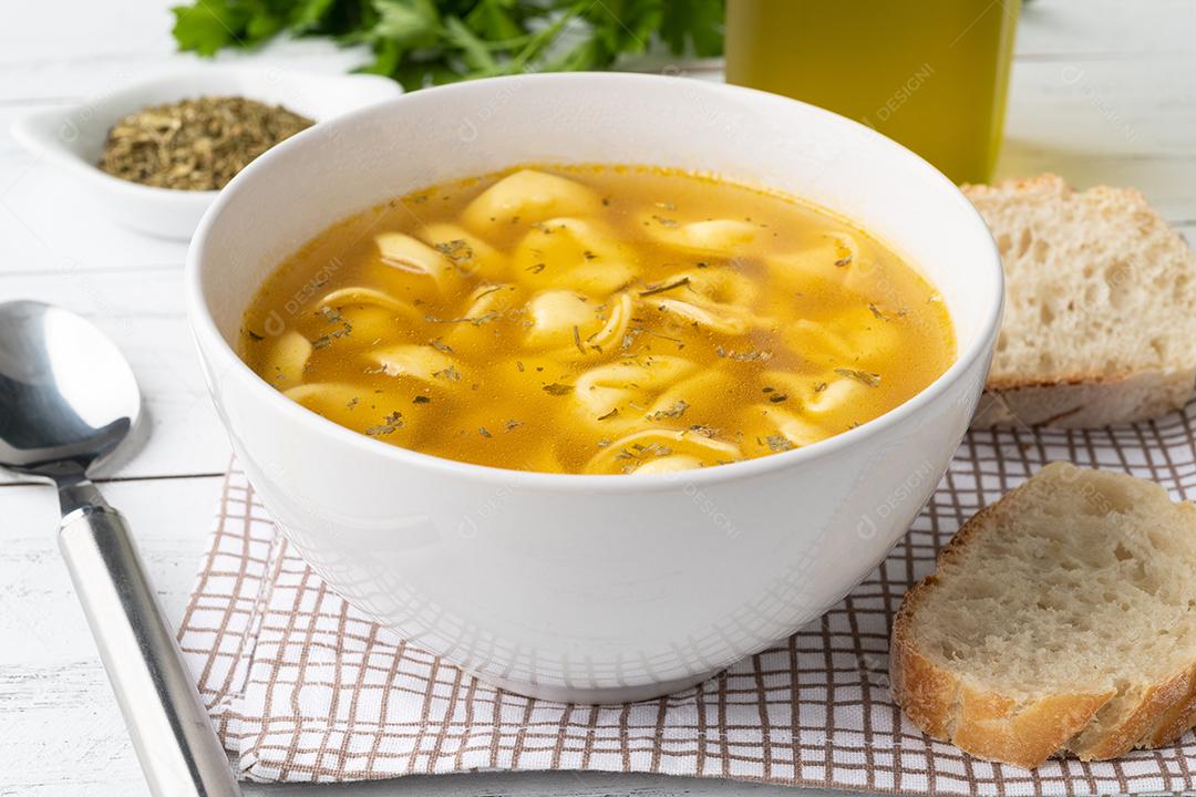 Sopa de cappelletti ou tortellini brodo em uma tigela com fatias de pão