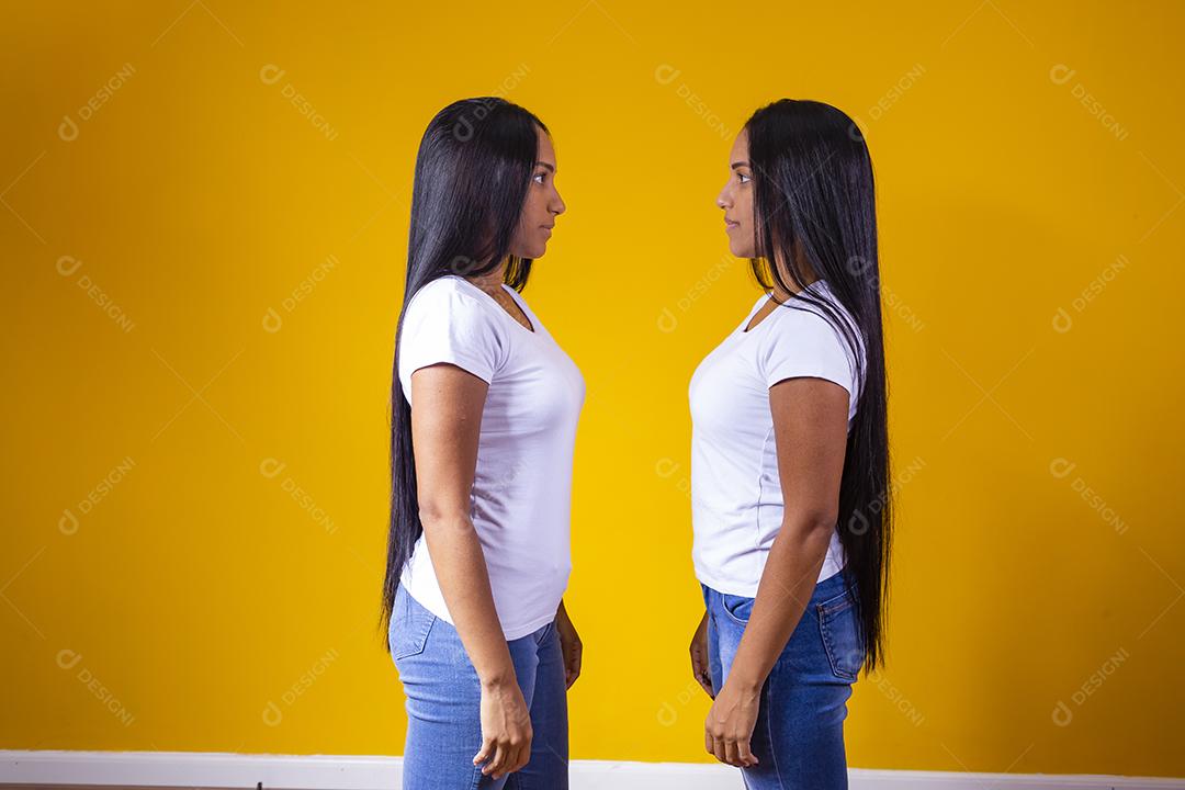 Duas mulheres irmãs gêmeas olhando uma para outra em fundo amarelo