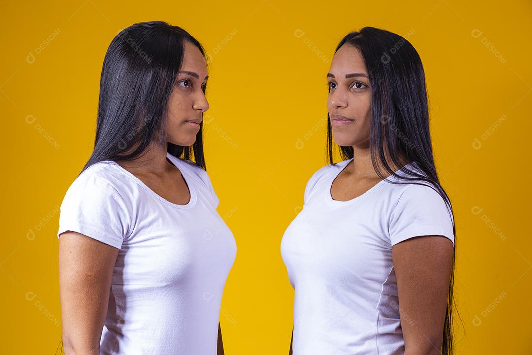Duas mulheres irmãs gêmeas olhando uma para outra em fundo amarelo