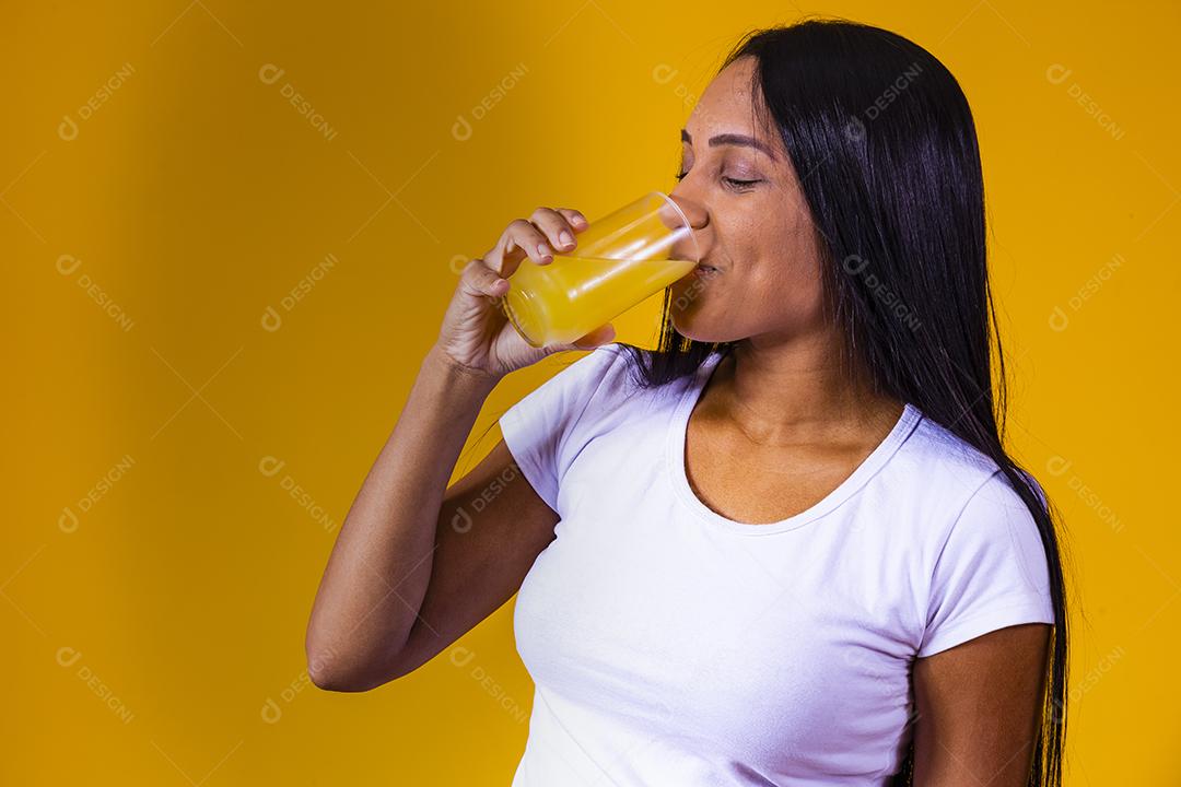 mulher bebendo suco de laranja em fundo amarelo