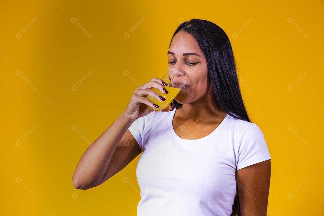 mulher bebendo suco de laranja em fundo amarelo