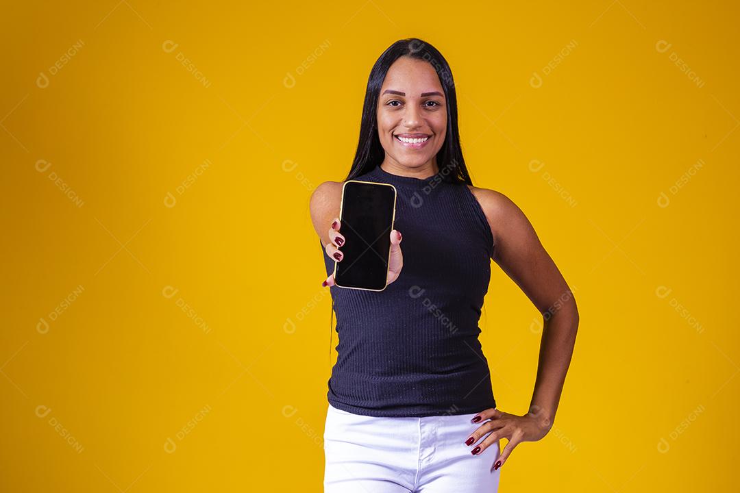 Jovem morena segurando um celular com tela em branco para texto em fundo amarelo