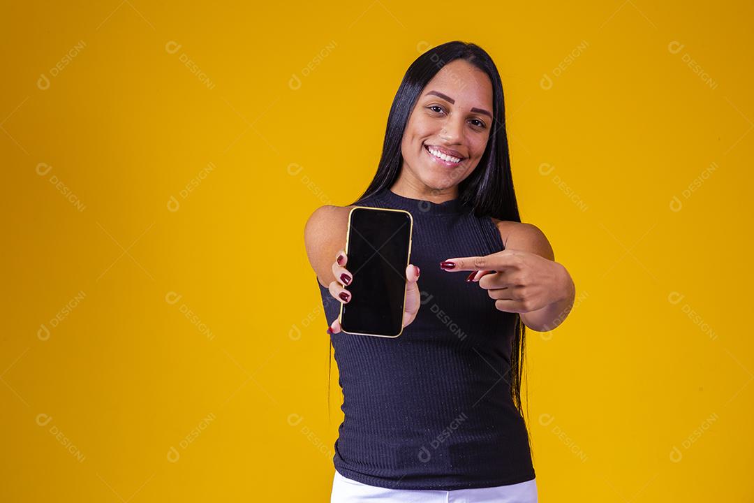 Jovem morena segurando um celular com tela em branco para texto em fundo amarelo