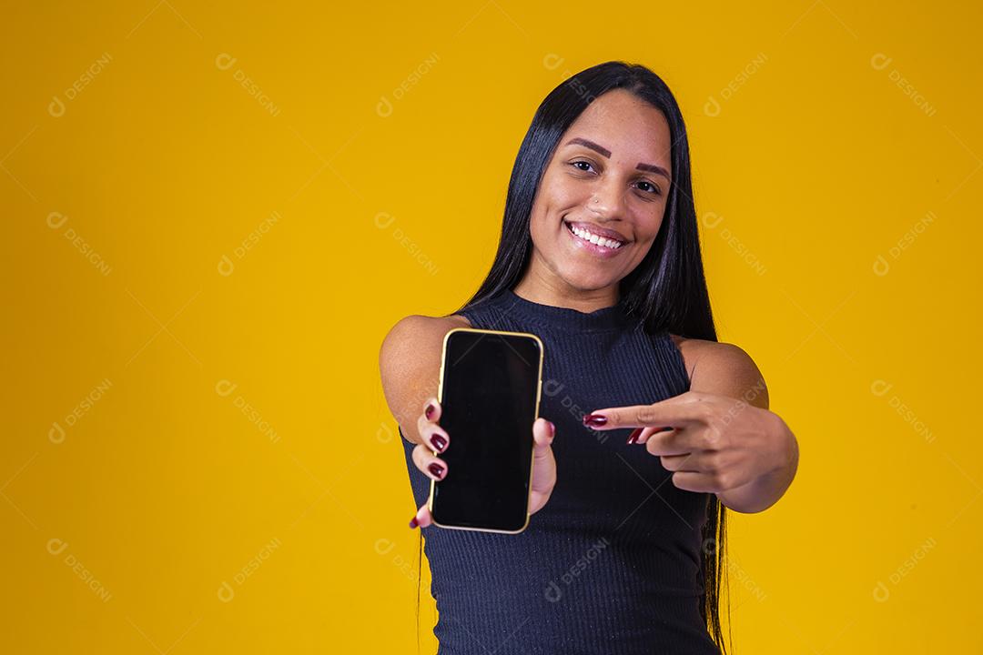 Jovem morena segurando um celular com tela em branco para texto em fundo amarelo