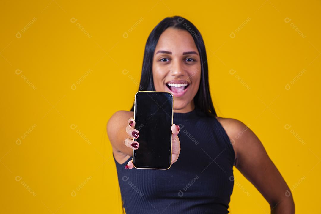 Jovem morena segurando um celular com tela em branco para texto em fundo amarelo