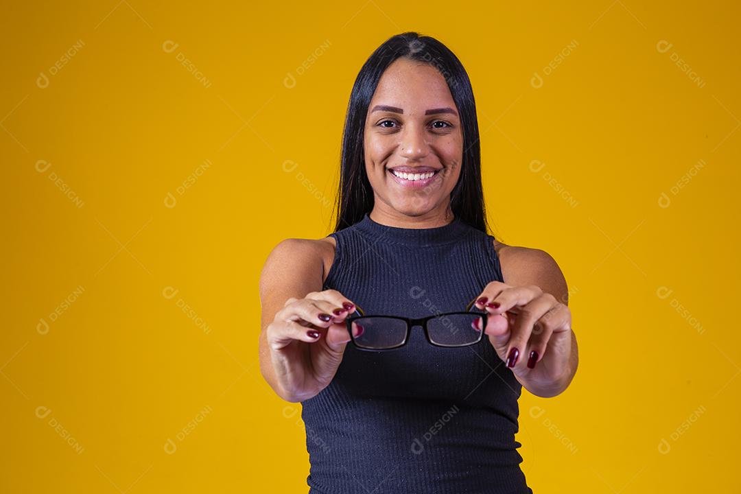 Mulher jovem e bonita com cabelo comprido, usando óculos e braços cruzados sobre fundo amarelo