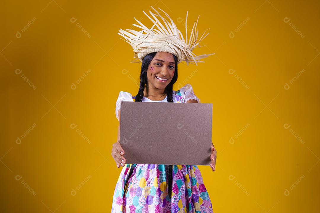 Linda mulher vestida com roupa de festa junina segurando uma placa em branco