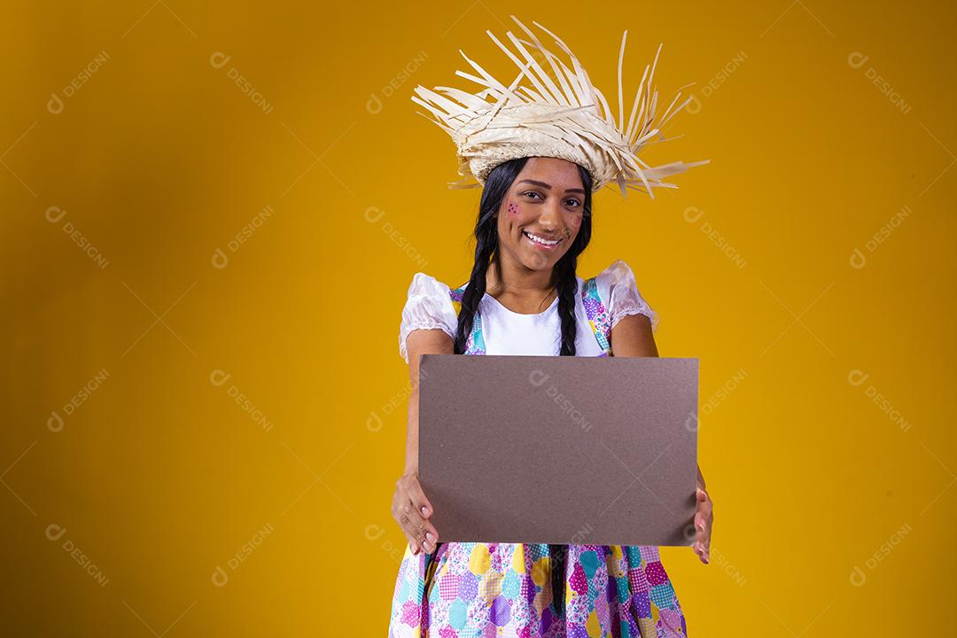 Linda mulher vestida com roupa de festa junina segurando uma placa em branco