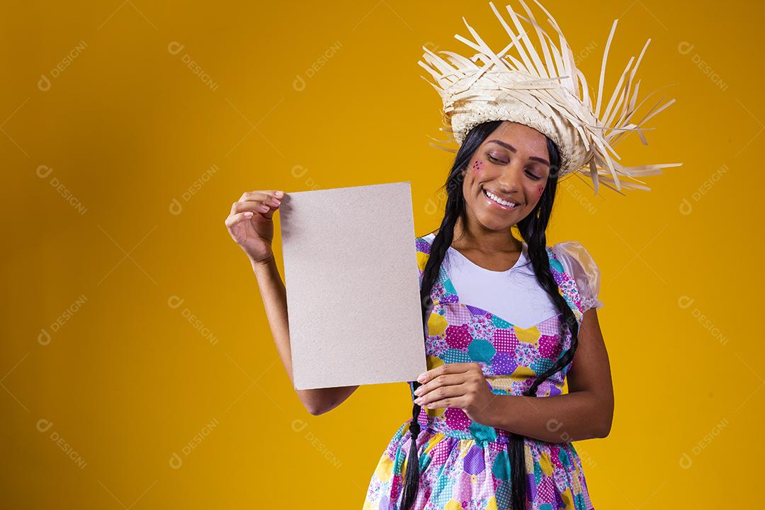 Linda mulher vestida com roupa de festa junina segurando uma placa em branco