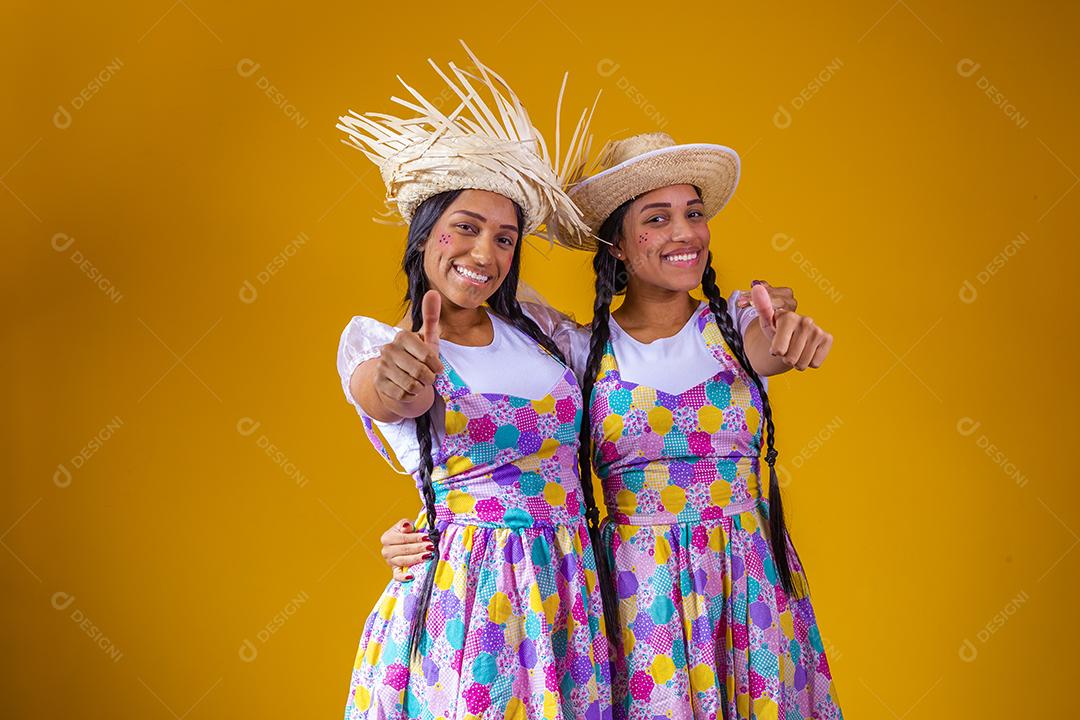 jovens irmãs gêmeas com polegar para cima e roupas de festa junina