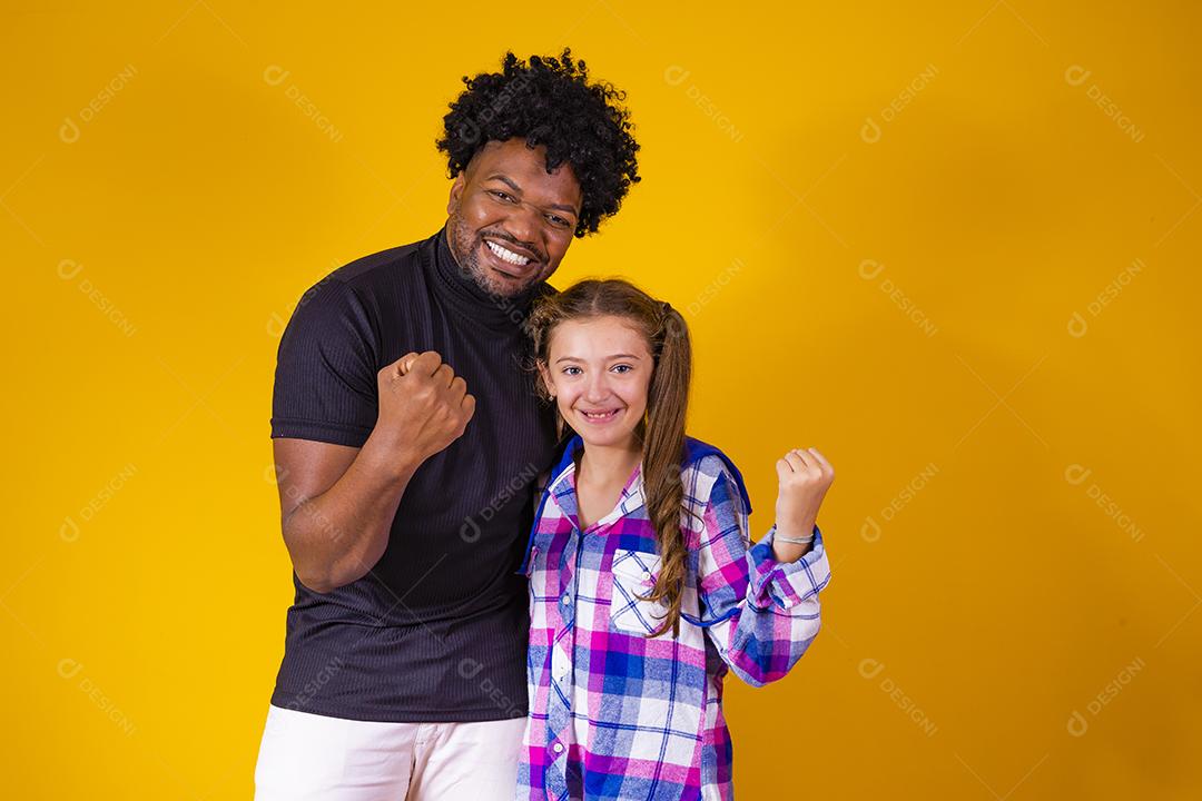 pai e filha em fundo amarelo comemorando a vitória. Pai e filha fazendo sinal de sim