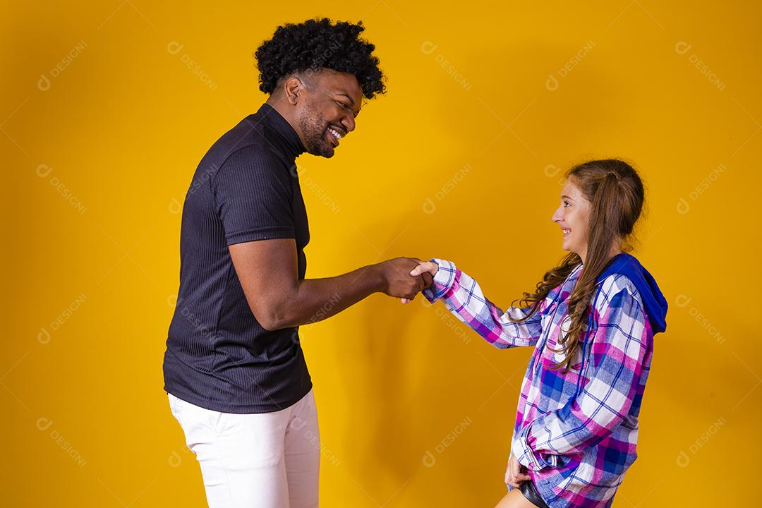 Pai dando a mãos para filhas sobre fundo amarelo