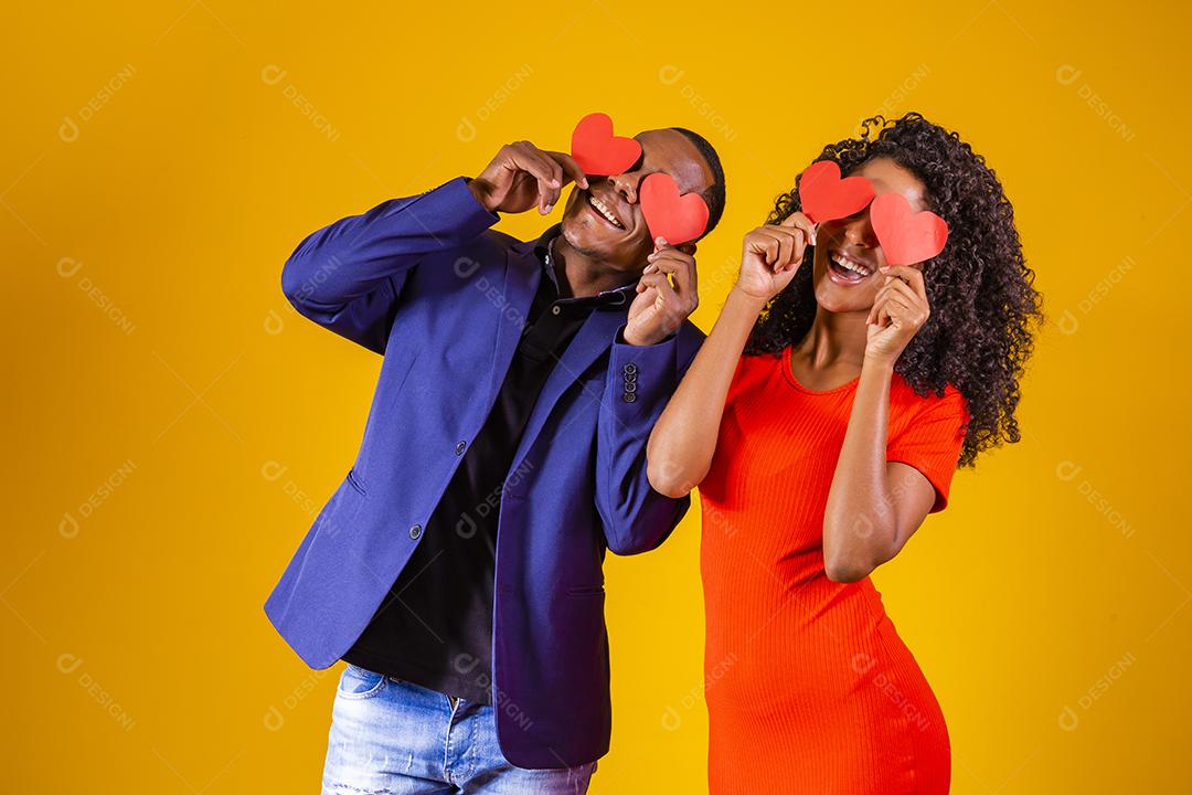 Feliz casal jovem está segurando corações de papel vermelho e sorrindo, em fundo amarelo