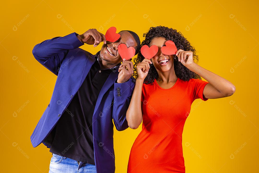 Feliz casal jovem está segurando corações de papel vermelho e sorrindo, em fundo amarelo