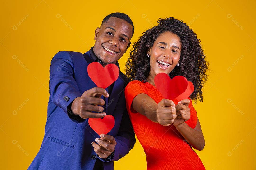 Feliz casal jovem está segurando corações de papel vermelho e sorrindo, em fundo amarelo