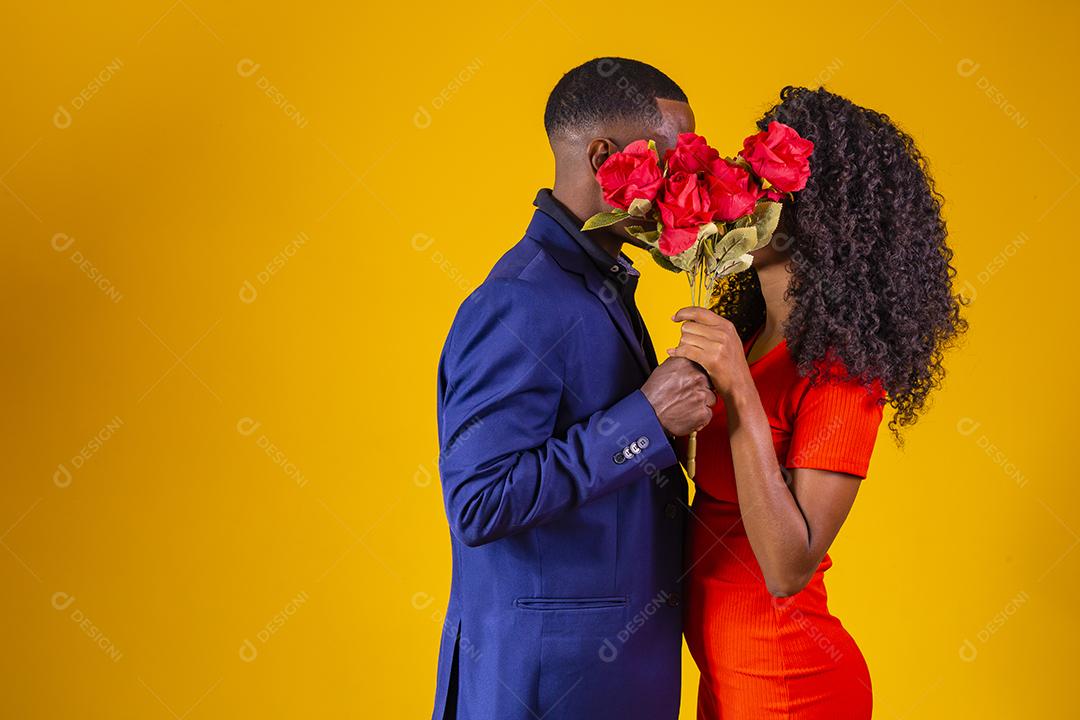 Lindo casal elegante está se beijando atrás de rosas, em fundo amarelo