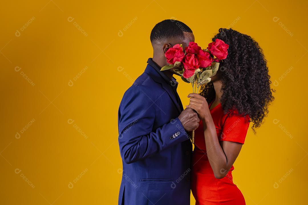 Lindo casal elegante está se beijando atrás de rosas, em fundo amarelo