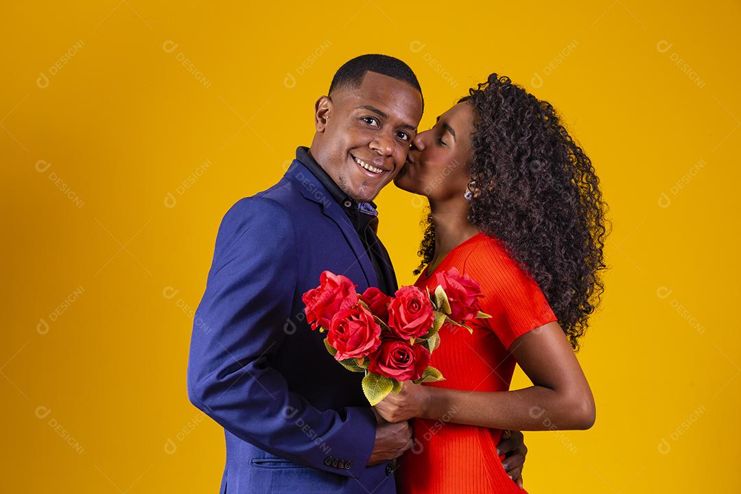 Lindo casal romântico isolado em fundo amarelo. Mulher jovem e atraente de vestido vermelho segurando rosas vermelhas