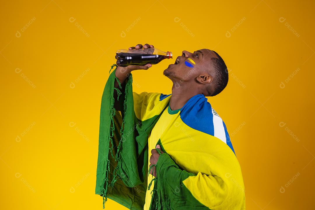 Homem afro, fã brasileiro, bebendo um líquido preto de uma garrafa. homem fã brasileiro com refrigerante de cola