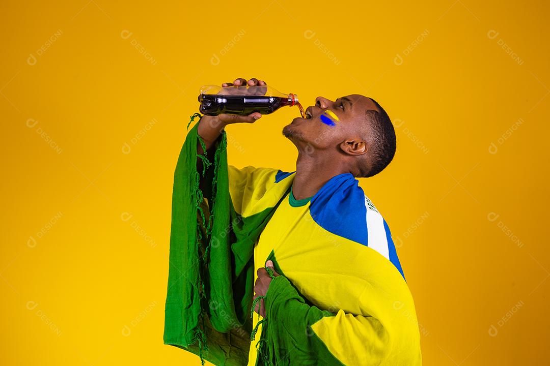 Homem afro, fã brasileiro, bebendo um líquido preto de uma garrafa. homem fã brasileiro com refrigerante de cola